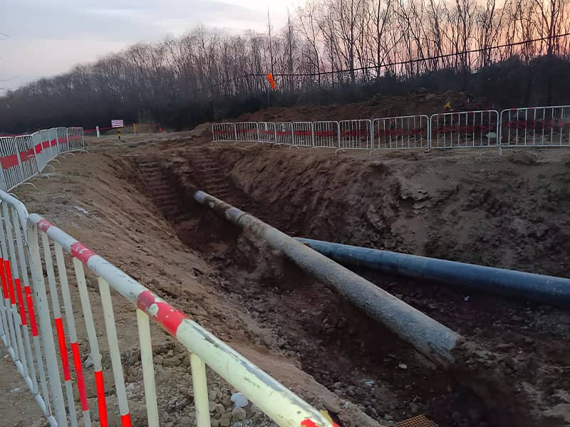 Excavated trench with laid pipelines, enclosed by safety barriers at Suqian natural gas pipeline relocation construction site