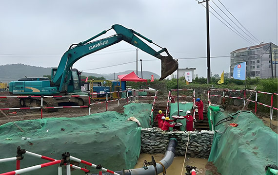 Workers operating equipment in enclosed excavation pit during petroleum pipeline repair, part of pipeline shutdown operation and hot tapping and plugging process
