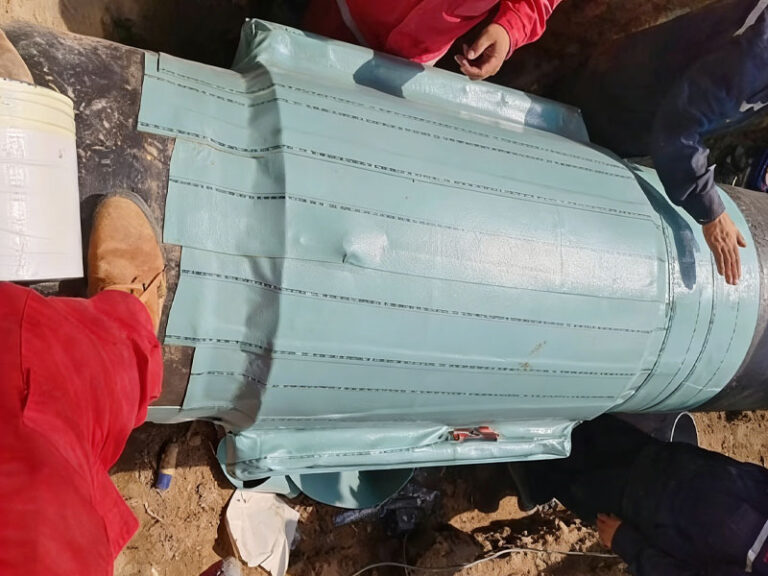 Workers apply a protective repair sleeve to an excavated pipeline in a trench, addressing damage from pipeline deterioration to restore functionality.