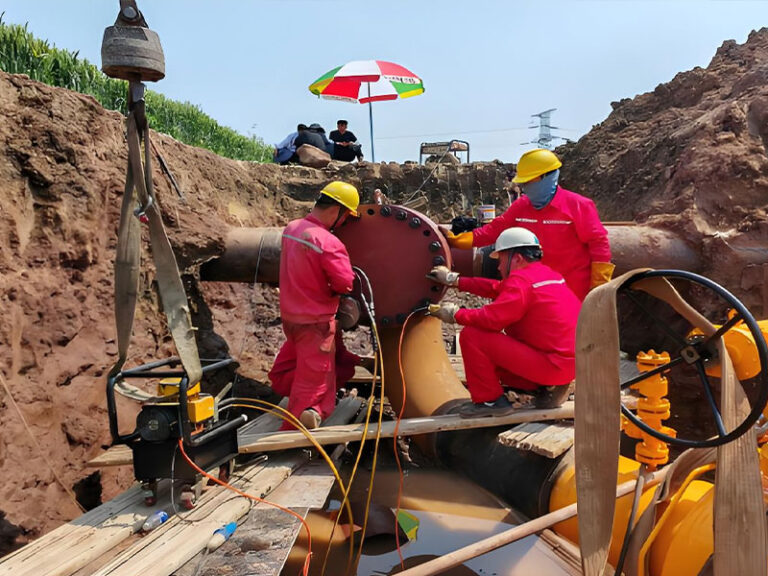 Workers installing fittings for natural gas pipeline hot tapping on in-service pipeline, in excavation pit with construction gear
