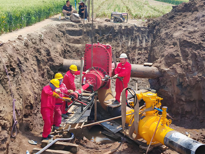 Workers adjusting red hot tapping equipment connected to in-service natural gas pipeline, during live pipeline connection and hot tapping project