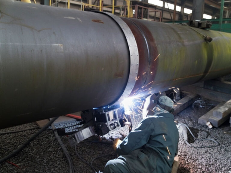 A professional welder using automated orbital welding equipment on a large-diameter industrial pipeline with bright sparks and protective gear.