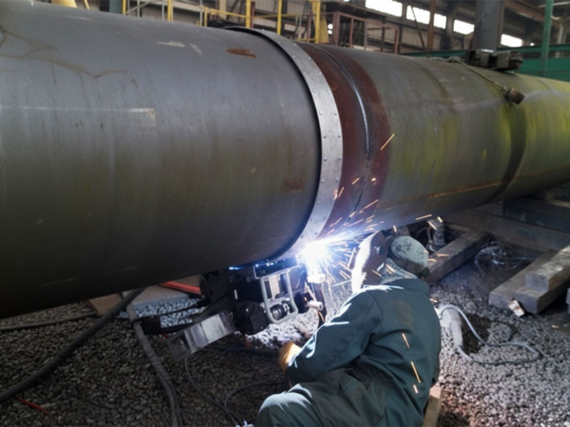 Un soudeur professionnel utilisant un équipement de soudage orbital automatisé sur une canalisation industrielle de grand diamètre, avec des étincelles vives et équipé d'un équipement de protection.