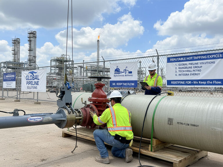 Two professional technicians in high-visibility safety gear performing a hot tapping procedure on a large industrial pipeline at a refinery facility, featuring Global Pipeline Solutions signage.