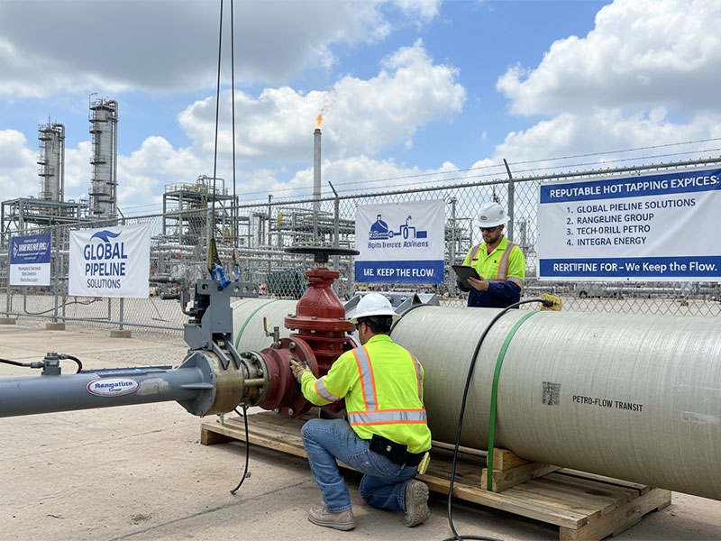 Deux techniciens professionnels en tenue de sécurité haute visibilité effectuant une procédure de taraudage à chaud sur un grand pipeline industriel dans une raffinerie, avec la signalisation de Global Pipeline Solutions.