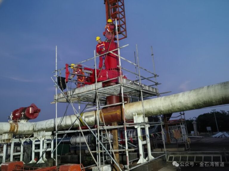 Professional team performing a hot tapping operation on a large industrial pipeline from a metal scaffolding structure at dusk.