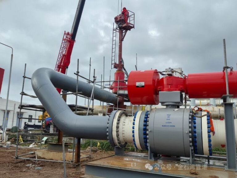 A professional hot tapping pipeline service site featuring a large grey industrial pipeline with a red valve actuator and scaffolding for maintenance work.