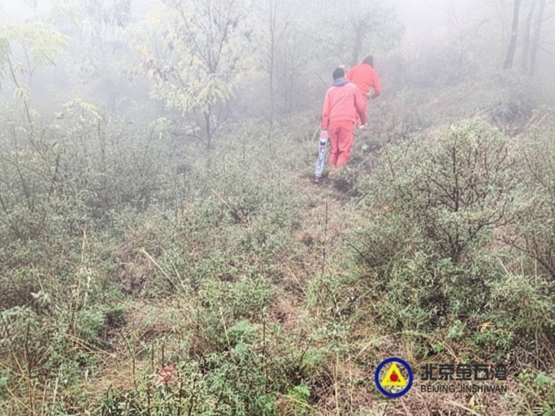 Two inspectors in orange protective gear walking through a foggy, brush-covered field to perform a PMT non-contact magnetic stress inspection for underground pipeline safety.