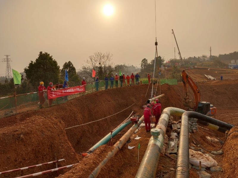 anhe-aviation-fuel-pipeline-relocation-plugging-construction-xuzhou Construction workers in red safety uniforms performing pipeline plugging for the Anhe aviation fuel pipeline relocation project at a construction site in Xuzhou with an excavator and crane visible during sunset.