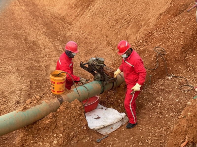 dn250-aviation-kerosene-pipeline-sealing-technical-service Two professional workers in red protective gear and helmets perform technical sealing on a DN250 aviation kerosene pipeline during a relocation construction project.
