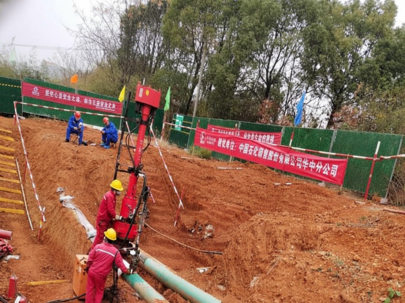 dn250-jet-fuel-pipeline-plugging-hot-tapping-service Professional engineering team performing a DN250 jet fuel pipeline plugging and hot tapping service at a construction site for a pipeline relocation project, featuring specialized red drilling equipment.