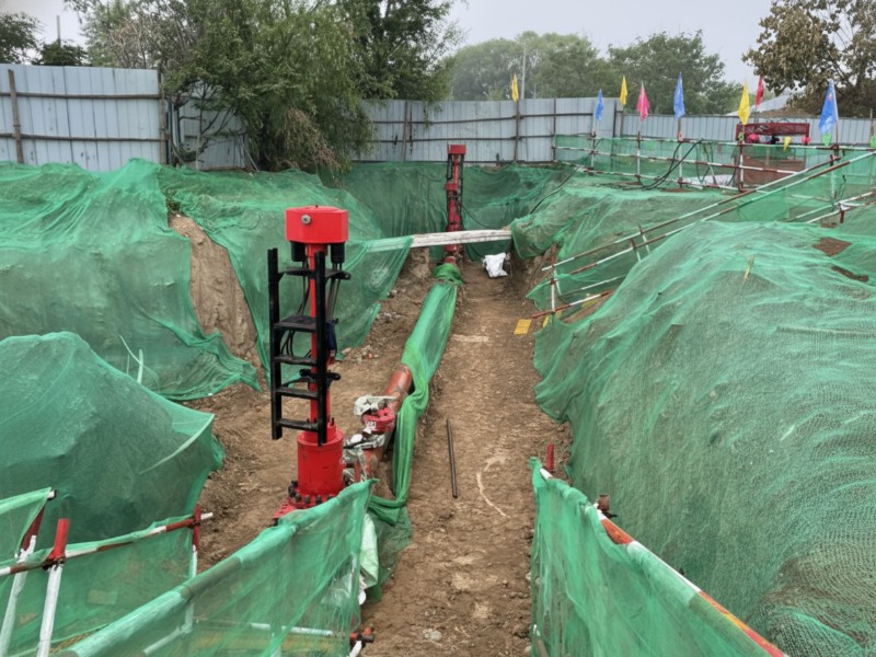 An industrial construction site for pipeline relocation and maintenance, featuring red flow-stopping plugging equipment and excavated trenches protected by green safety netting.