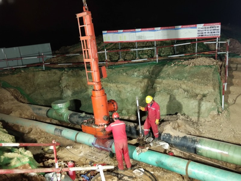 Workers in red safety gear performing hot tapping and line plugging on a large-diameter oil pipeline during a relocation project at night in Anhui Province.