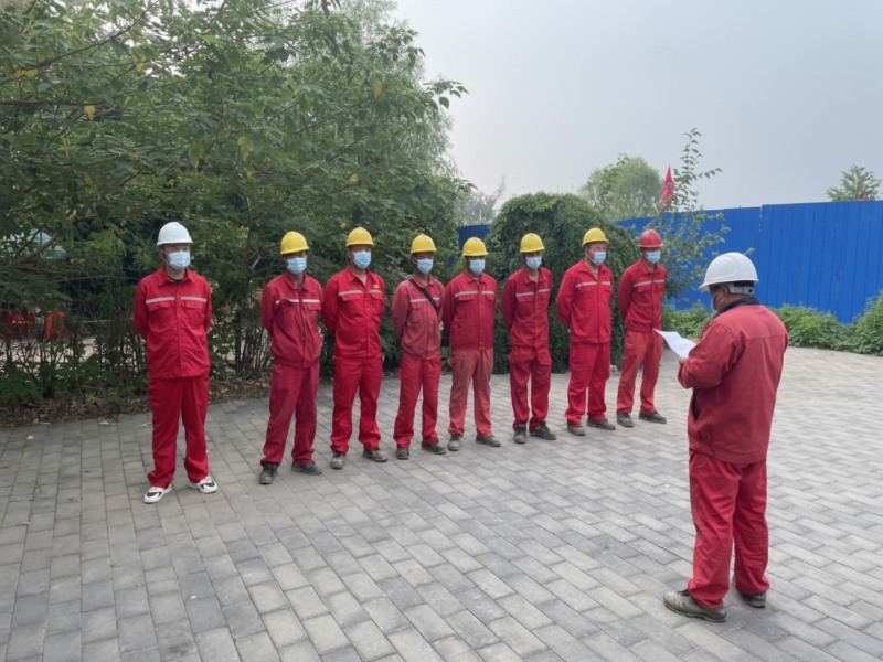 A team of construction workers in red overalls and hard hats attending a safety briefing for a pipeline project involving plugging, oil drainage, and tie-in operations.