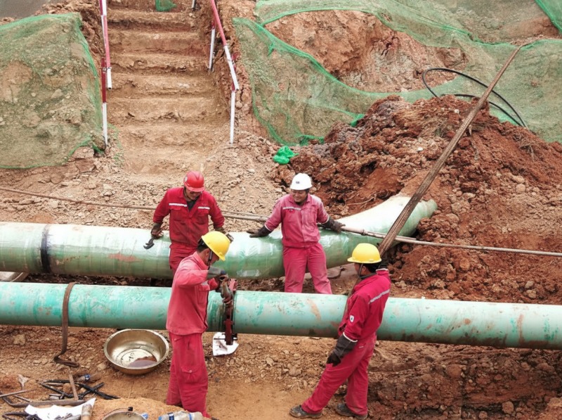 Construction workers in red uniforms and safety helmets performing relocation and hot tapping on DN400 and DN250 oil pipelines at the Anhe and Anhao railway crossing project in Anhui.