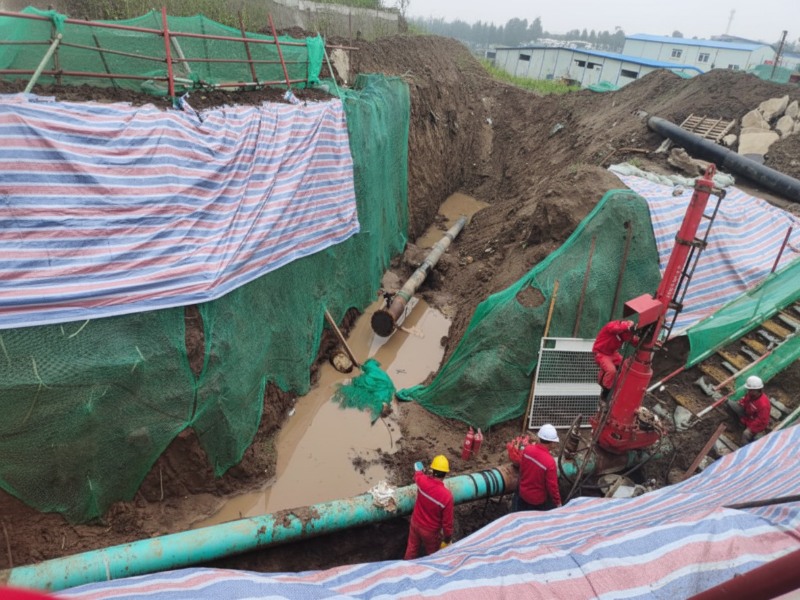 Construction crew in red uniforms performing hot tapping, pipeline tie-in, and old line removal operations at a large-scale excavation site with protective netting and mud.