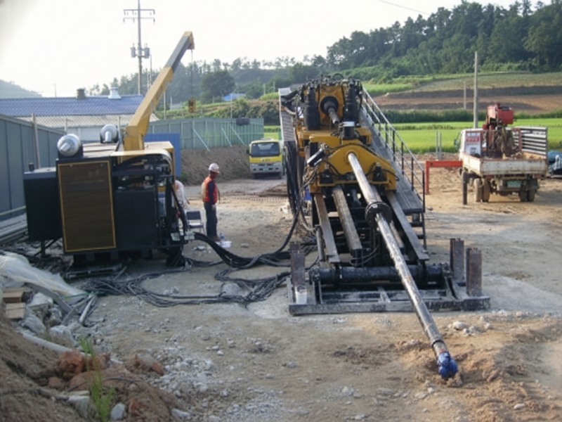 A yellow Drillto horizontal directional drilling rig being operated by construction workers in safety vests and hard hats at a muddy trenchless construction site.