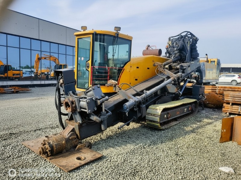 A large yellow crawler-mounted horizontal directional drilling (HDD) machine parked on a gravel yard, featuring a glass operator's cab and drilling assembly for trenchless construction.