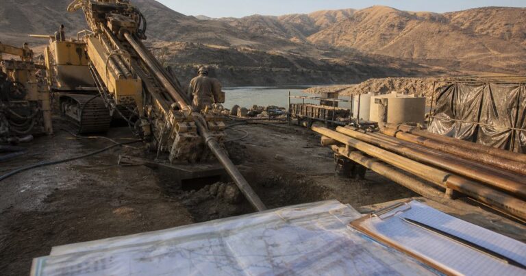 Horizontal directional drilling rig at a pipeline crossing site with risk planning documents in the foreground