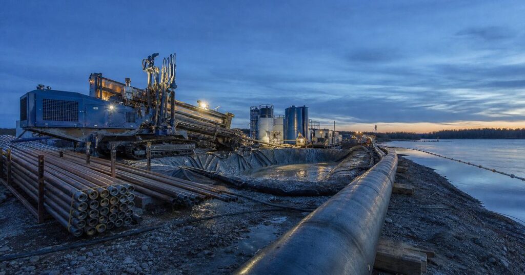 HDD rig at a river crossing entry pit with a pipe string laid out along the bank