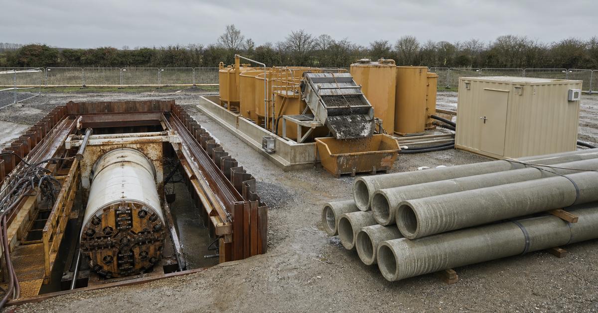 Microtunneling equipment spread on a construction site, showing a slurry shield machine at the launch shaft, separation plant tanks, control container and jacking frame staged on site