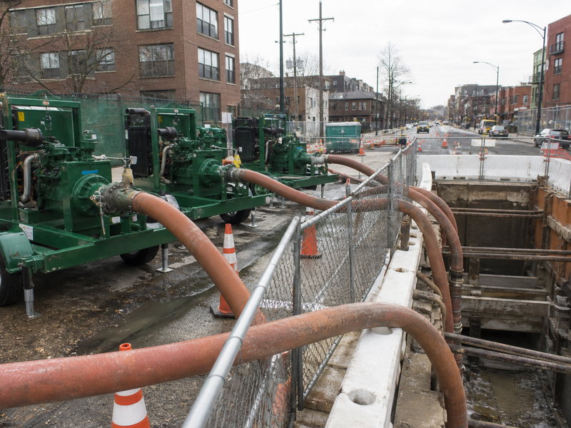 Temporary bypass pumping arrangement with hoses and pumps routing live sanitary flow around an active microtunneling shaft